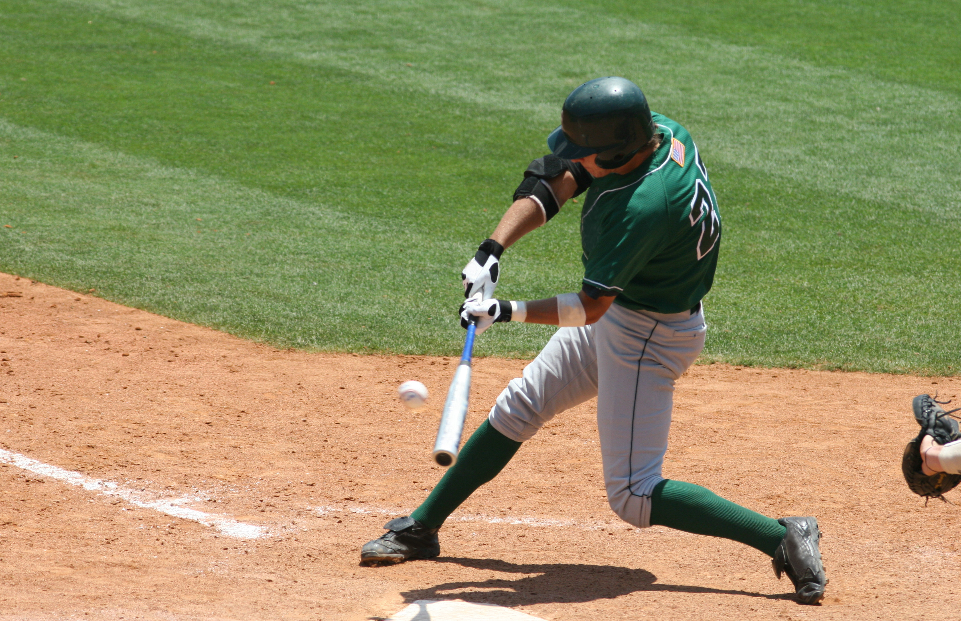 Baseball batter in green uniform hitting ball Baseball batter