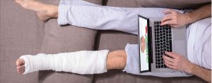 Man in cast on couch with laptop telemedicine